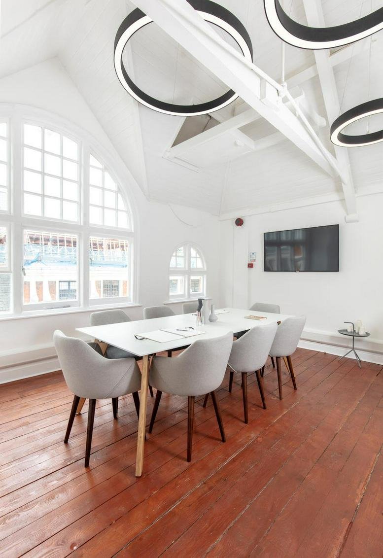 Bright boardroom with white table and grey chairs under circular halo light fixtures.