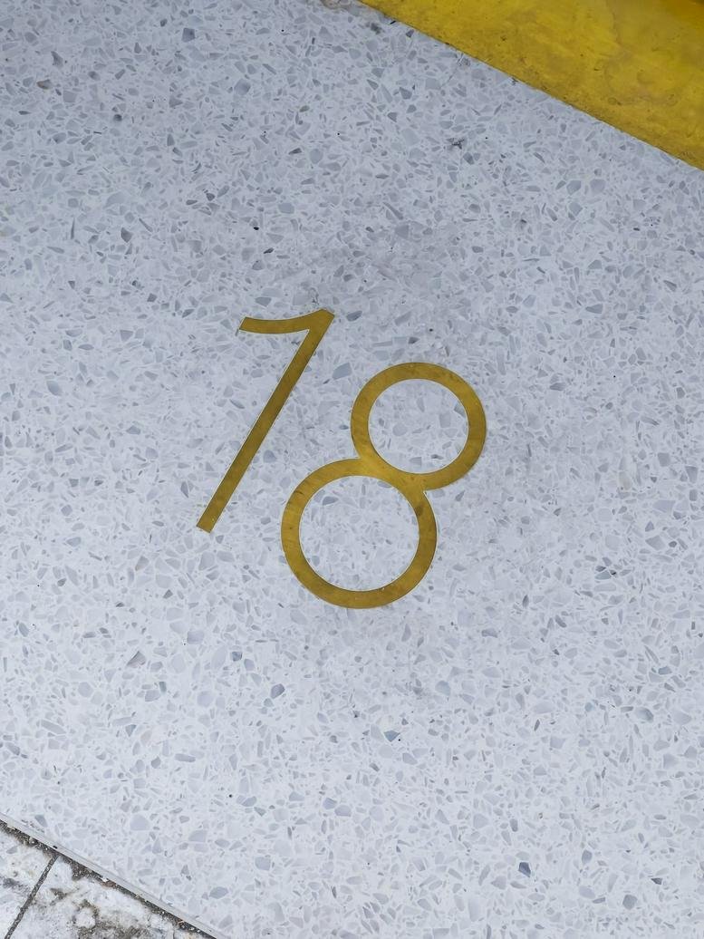 Close-up of the number 18 inlaid in brass on a light terrazzo floor.