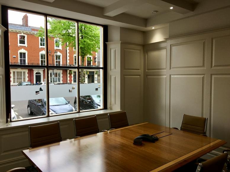 Bright boardroom with large windows overlooking a city street and paneled walls.