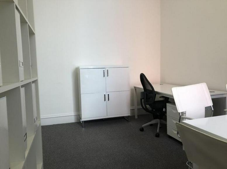 Clean, white-walled office with a white desk and ergonomic chair.
