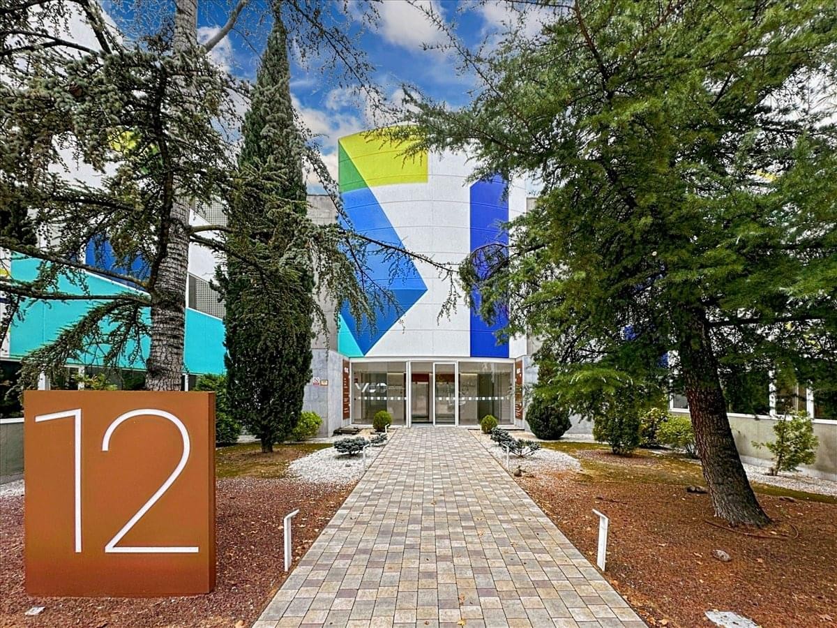 Exterior entrance of 2-16 Ronda del Poniente, Madrid with colorful geometric murals and paved walkway.