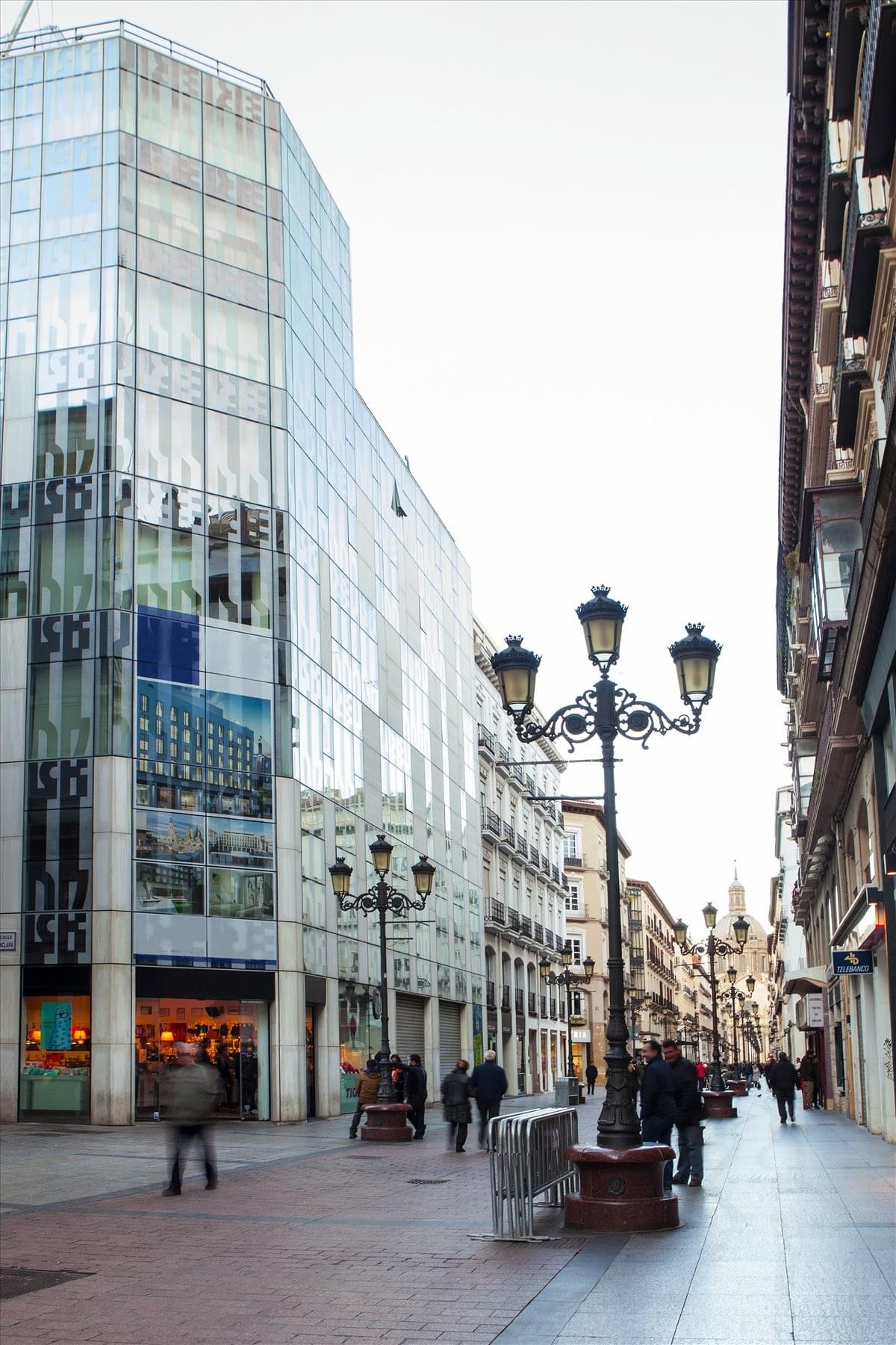 Modern glass building facade of NET ALFONSO I on a historic pedestrian street.