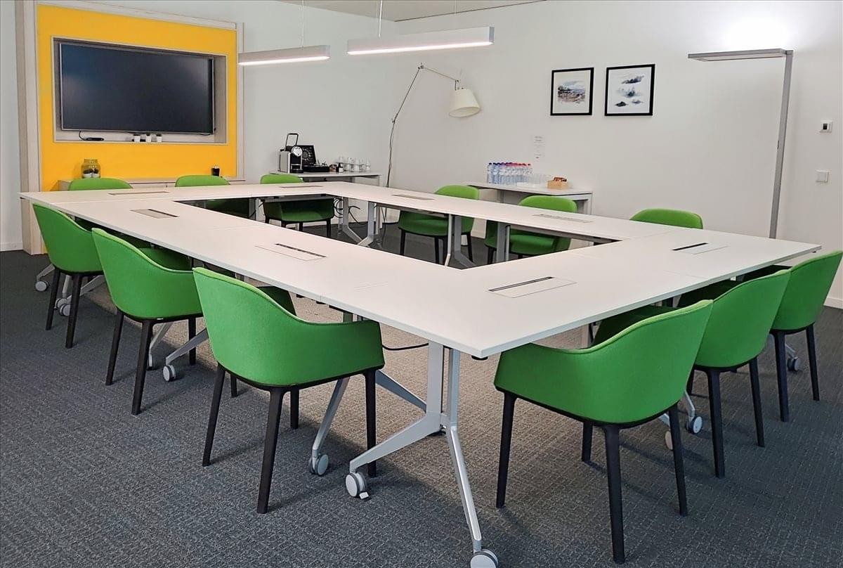 Large meeting room at the Oksigen Building with a hollow square table and vibrant green chairs.