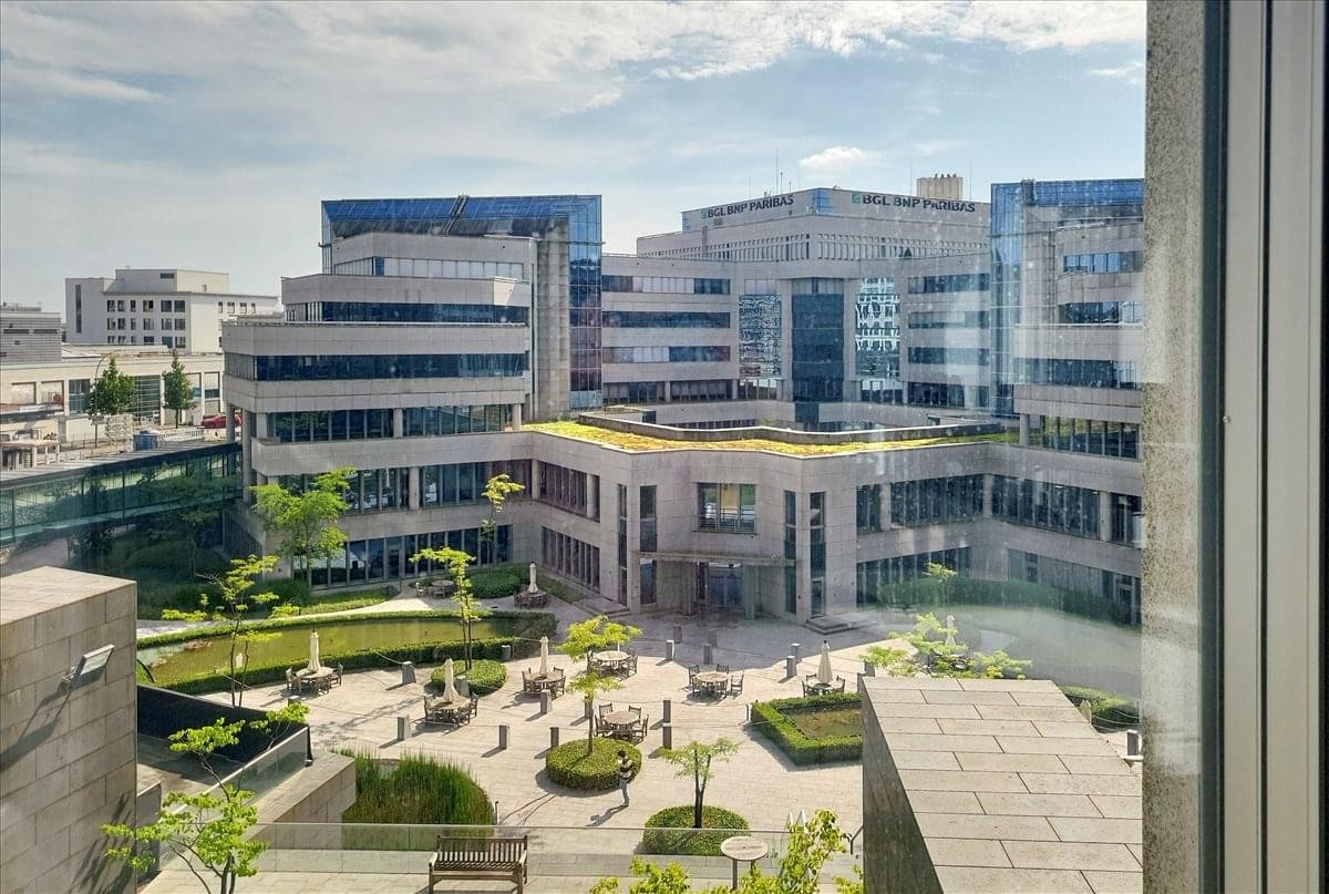 Elevated courtyard view of the Oksigen Building at 2 Rue Edward Steichen surrounded by greenery.