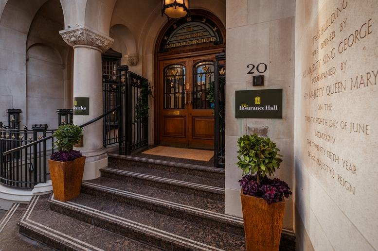 Grand stone entrance with double wooden doors and a dedicated building plaque.