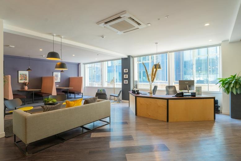 Spacious reception area with a curved wooden desk, lounge seating, and large windows with city views.