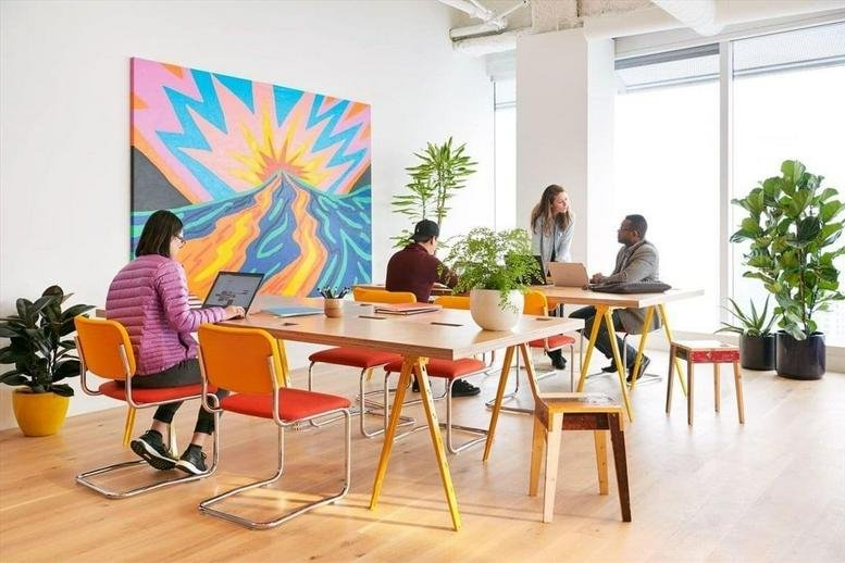 Sun-drenched coworking space at 21 Soho Square with a vibrant mural, large plants, and warm wooden tables.