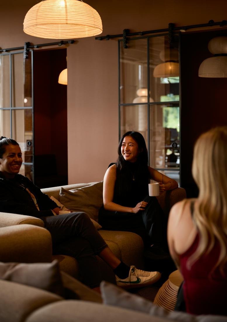 Coworkers enjoying a casual meeting on a comfortable sofa in a warm, lit breakout space.
