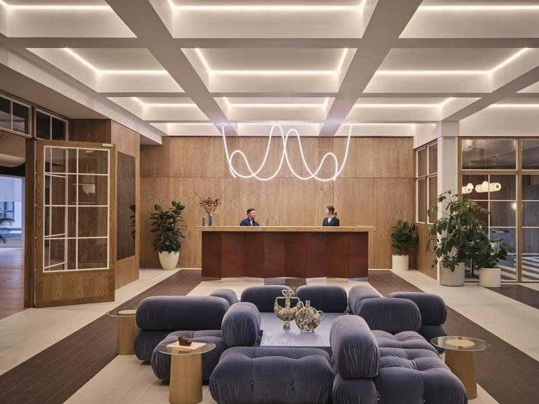 Grand reception lobby with a large wooden desk, grid-patterned ceiling lights, and blue velvet seating.