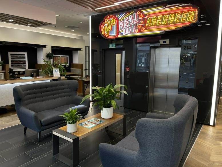 Modern reception area with grey sofas, wooden coffee table, and a vibrant neon sign.