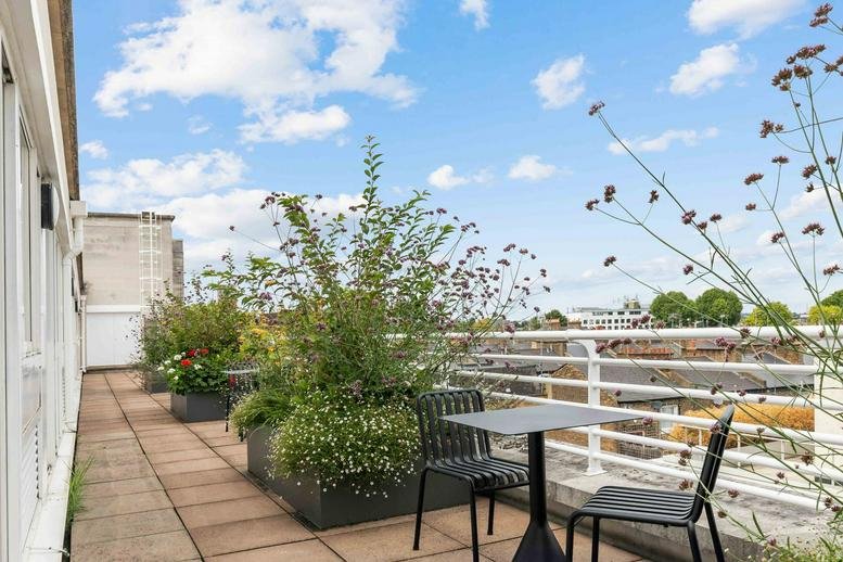 Sunny rooftop terrace with tables, chairs, and potted greenery at Glen House.