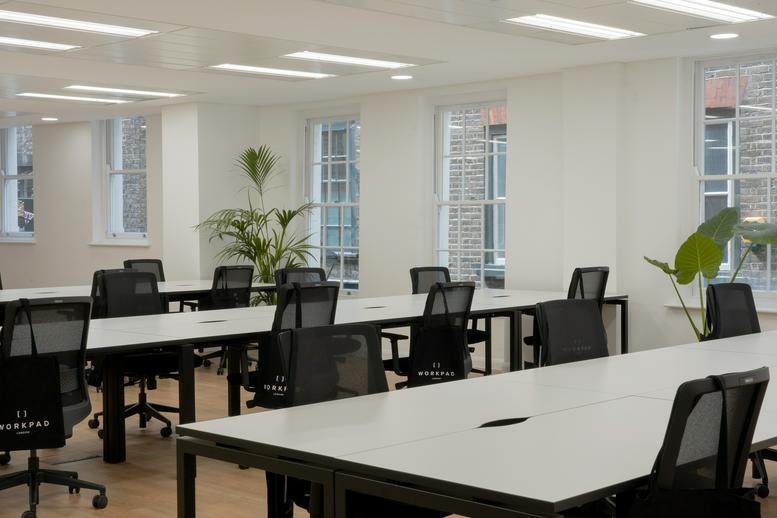 Spacious open-plan office with white desks, black chairs, and large windows.