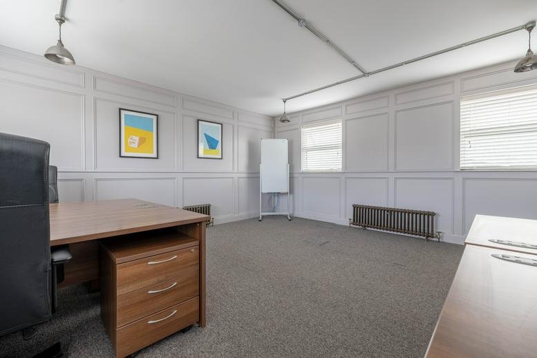 Spacious office room with grey paneled walls, wooden desk, and colorful wall art.