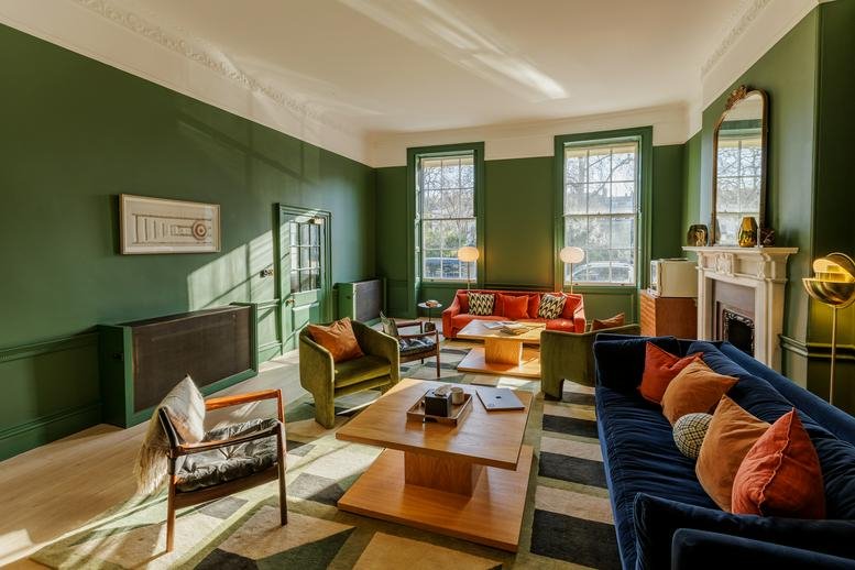 Elegant lounge area with forest green walls, plush seating, and large sash windows.