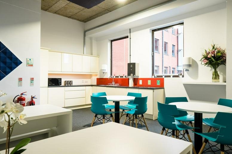 Spacious communal kitchen and dining area at 24-31 Shaftesbury Square with teal chairs and red accents.