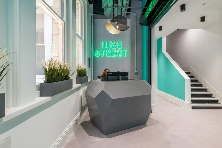 Modern reception area with a geometric grey desk and green neon signage for 24 Lime Street.