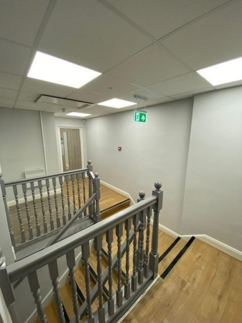 A staircase landing at 25 Mollison Avenue, Enfield featuring wood-style flooring and grey banisters.