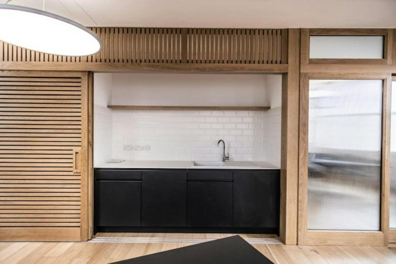 Communal kitchen area with black cabinetry and wooden slatted sliding doors.