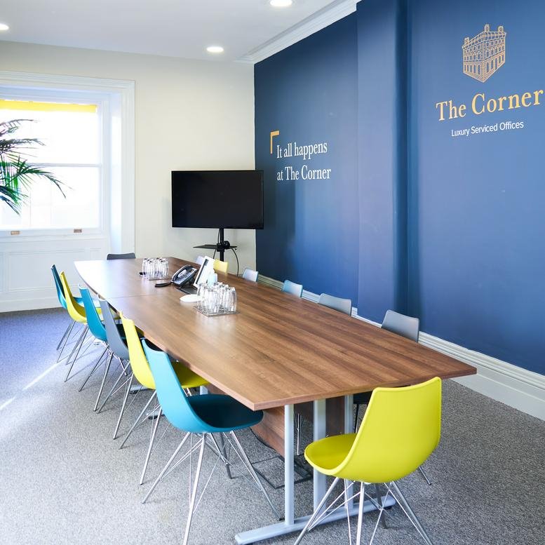 Spacious boardroom with a long wooden table, colourful chairs, and a blue feature wall.