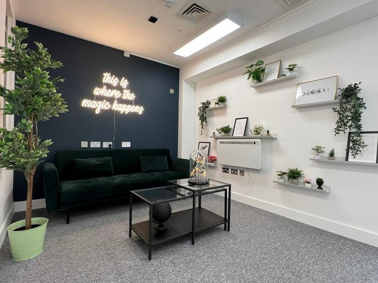 Lounge at Chelsea Chambers with green velvet sofa, neon wall sign, and numerous potted plants.