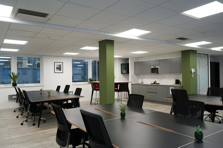Spacious open-plan coworking area with green pillars and a shared kitchen.