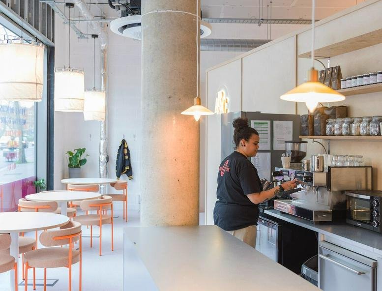 A vibrant cafe and breakout space at 272-274 Camberwell Road with a barista and modern hanging lights.