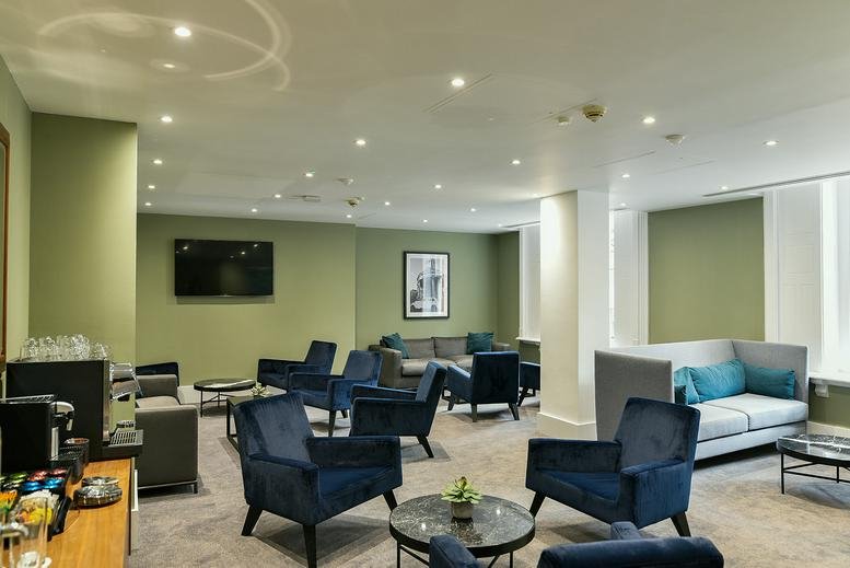 Lounge area featuring velvet blue armchairs, a television, and a coffee station.