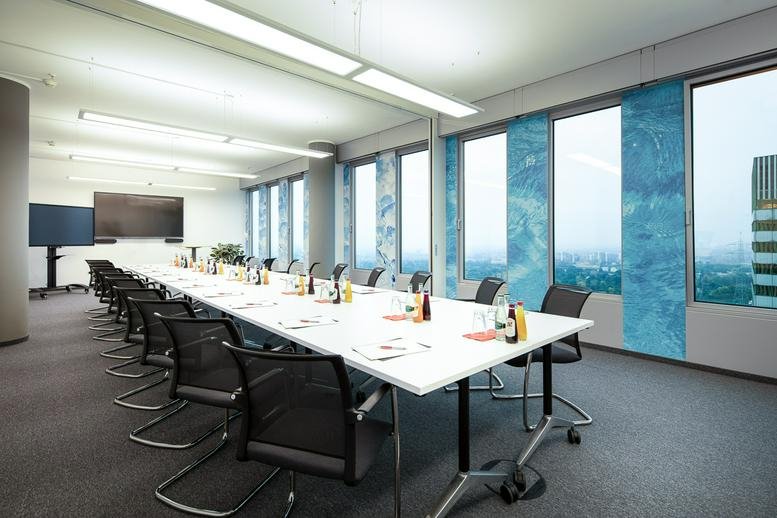 Long boardroom with a white conference table, black seating, and artistic blue window panels.