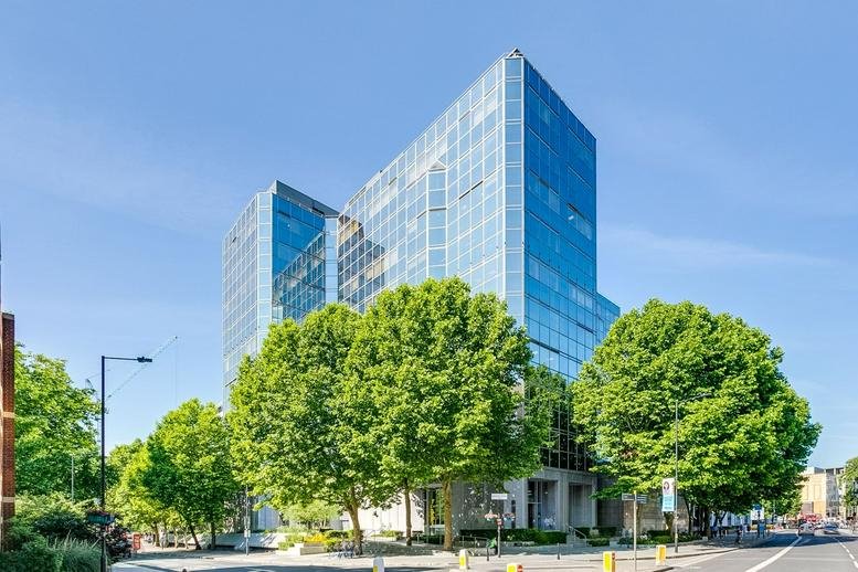 Exterior view of the modern glass-facade building at 3 Shortlands, Hammersmith, surrounded by green trees.