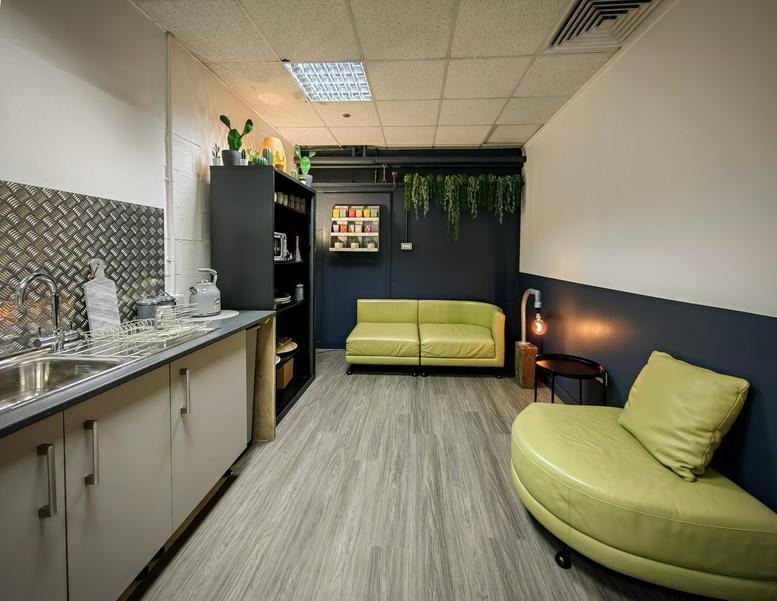 Spacious breakroom at 30-64 Pennywell Road with a kitchenette, green sofas, and hanging plants.