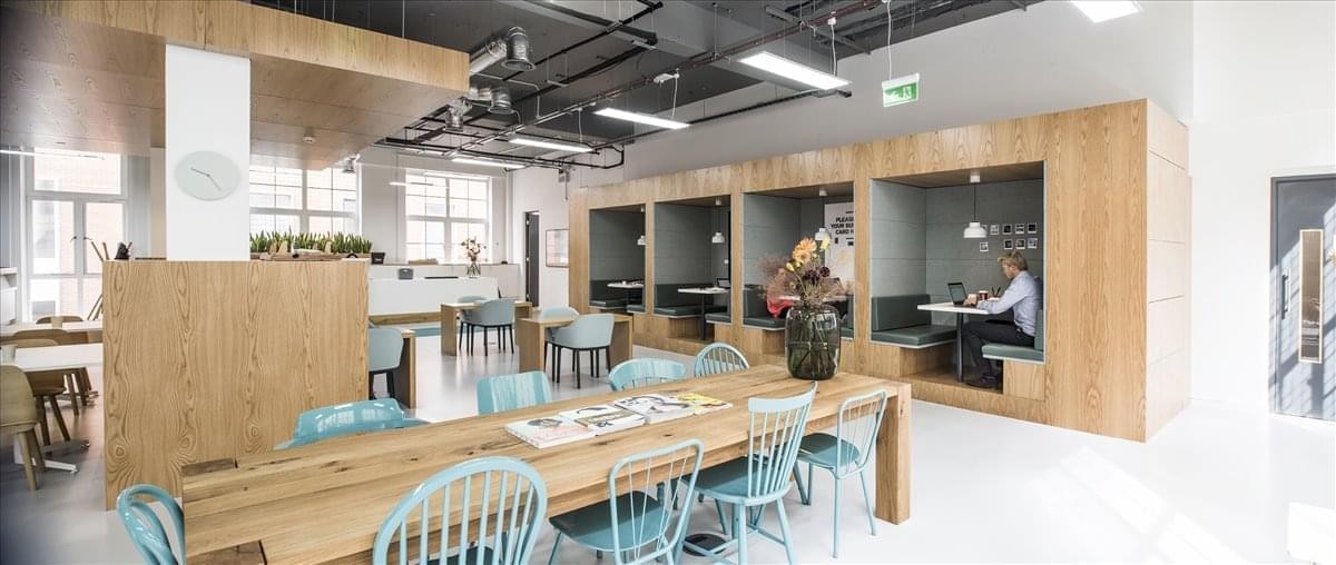 Spacious communal coworking area at 307 Euston Road with wooden tables, blue chairs, and private booths.