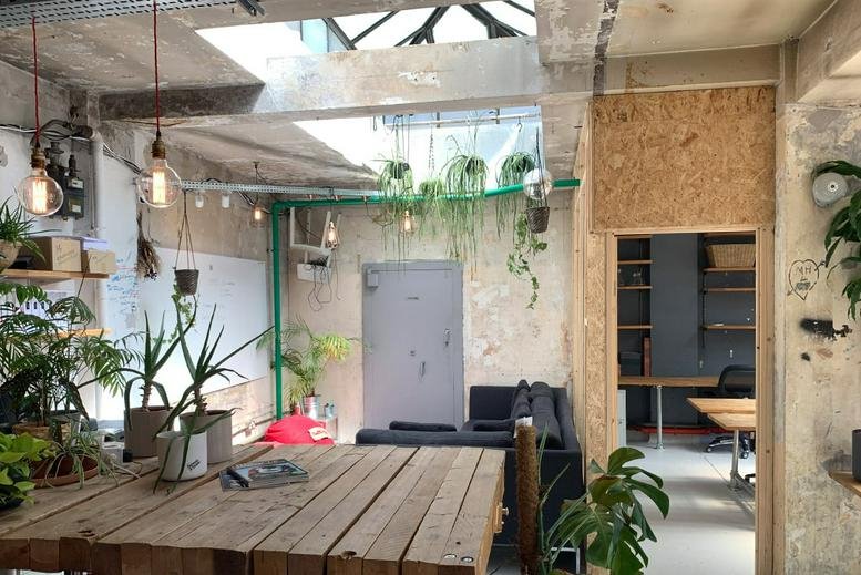 Communal breakout area with wooden tables, a black sofa, and hanging plants under a skylight at 34-35 Hatton Garden.
