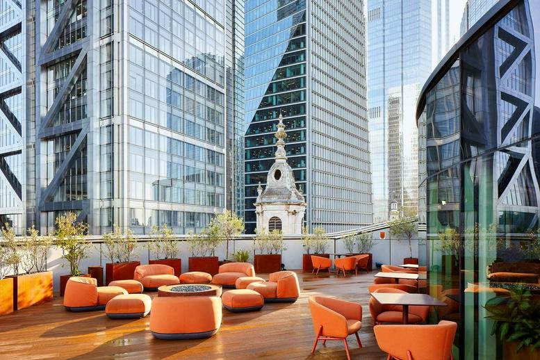Rooftop terrace with vibrant orange modular seating overlooking iconic city skyscrapers.