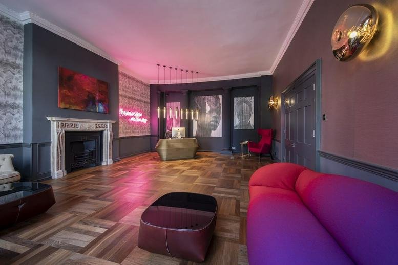 Reception lounge with a purple sofa, neon sign, and parquet flooring.