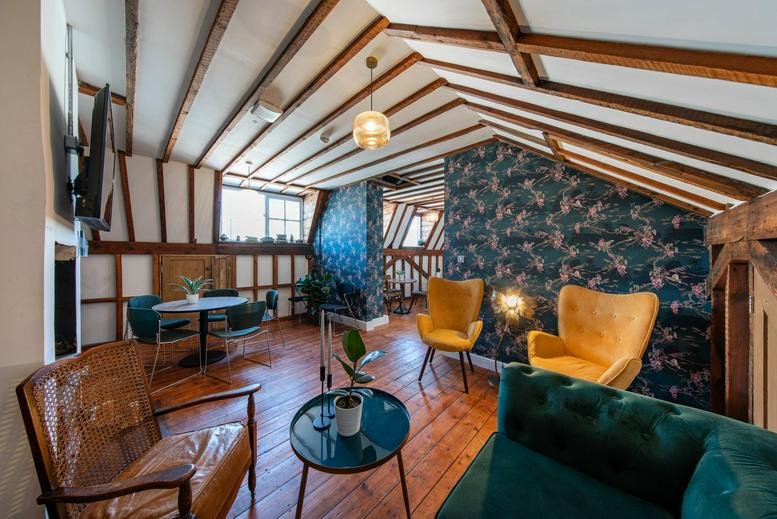 Characterful lounge at 385-389 Oxford Street with exposed beams, floral wallpaper, and velvet seating.