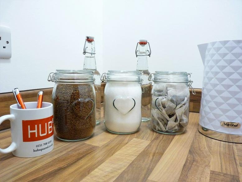 Communal kitchen area with coffee and tea canisters next to a white kettle.