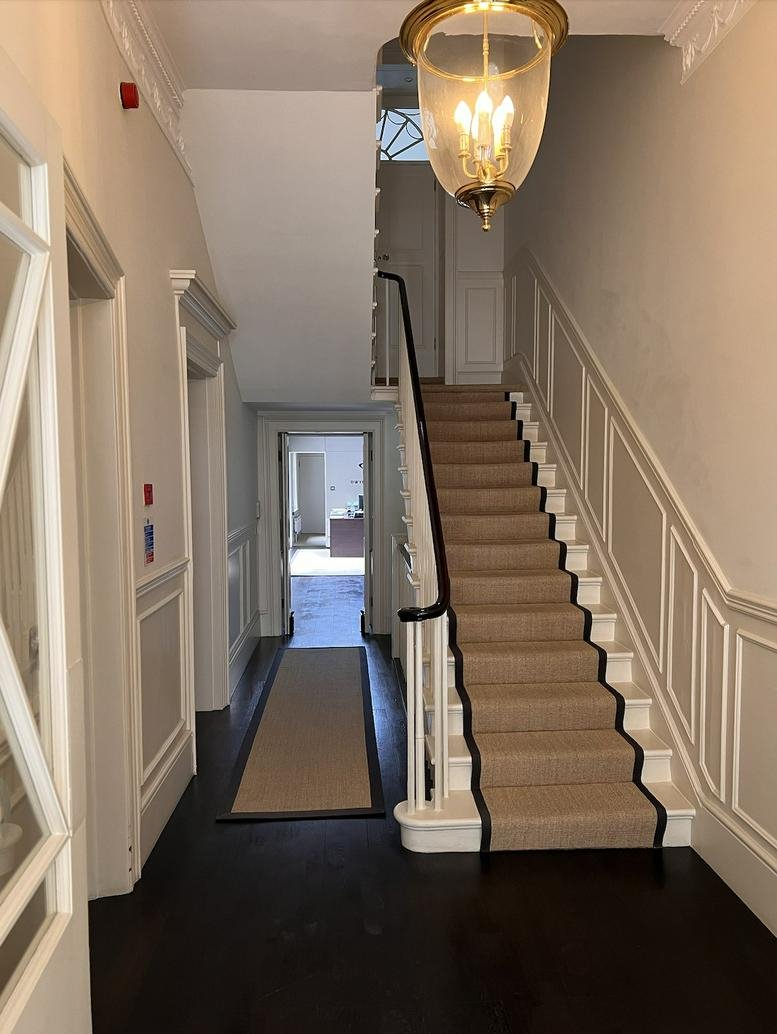 Grand staircase with wood floors, wall paneling, and a classic glass pendant light.