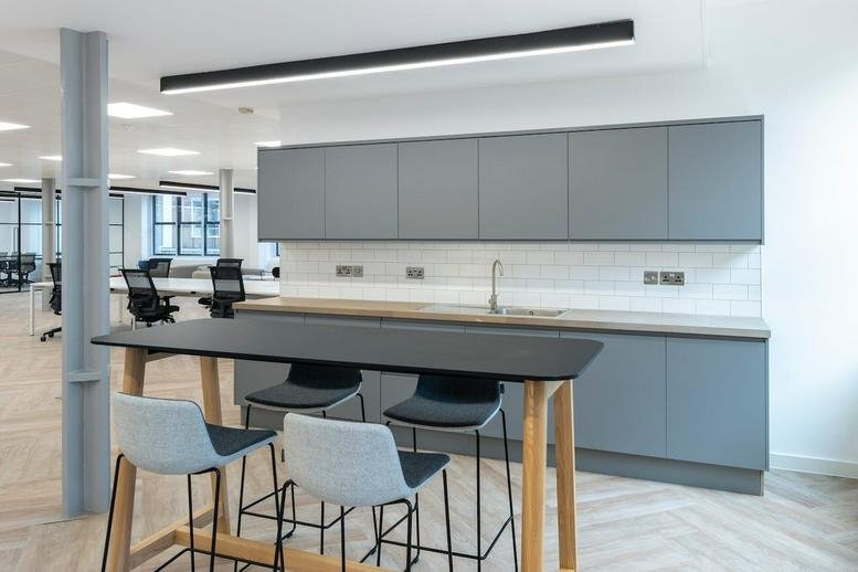 Modern office kitchen with sleek grey cabinetry, white tiled backsplash, and a high breakfast bar.