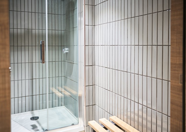 Modern shower cubicle with vertical grey tiling and a wooden bench.