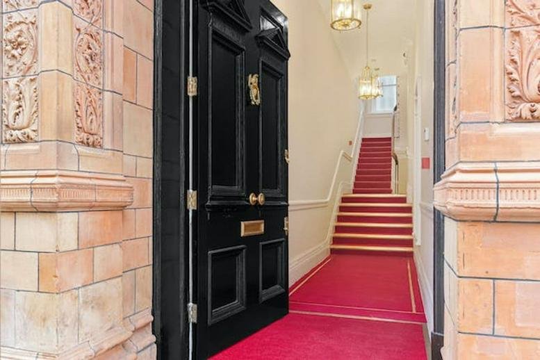 Entrance of 40, South Audley Street, London showing a black door and red carpeted stairs.