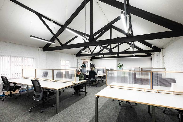 Open-plan office with white desks and black exposed roof trusses.