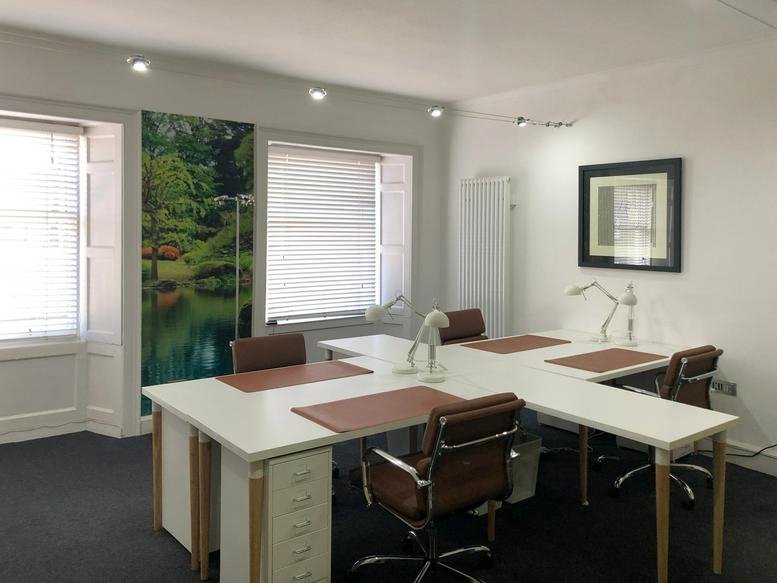 Open-plan office space with white desks and brown leather chairs.