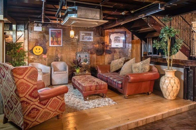 Lounge area at 47, 49 Camden Rd with leather sofas, patterned armchairs, and rustic wood-paneled walls.