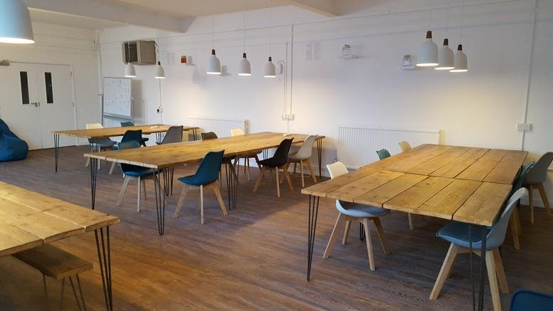 Spacious coworking area with long wooden tables and blue chairs at 47 Norfolk Street, Cambridge.