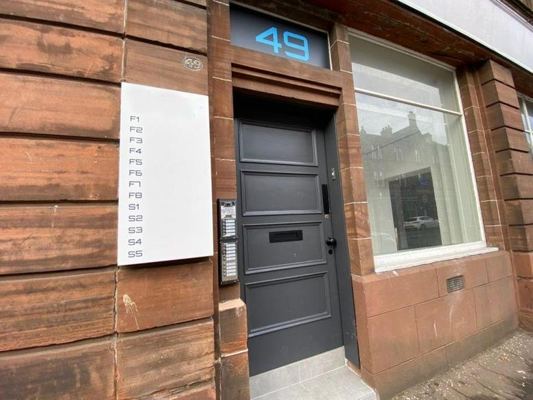 Exterior entrance of 49 John Finnie Street, Kilmarnock, East Ayrshire with dark grey door and sandstone facade.