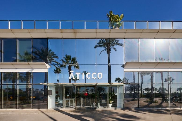 Exterior view of the glass-facade Aticco building showing reflected palm trees.
