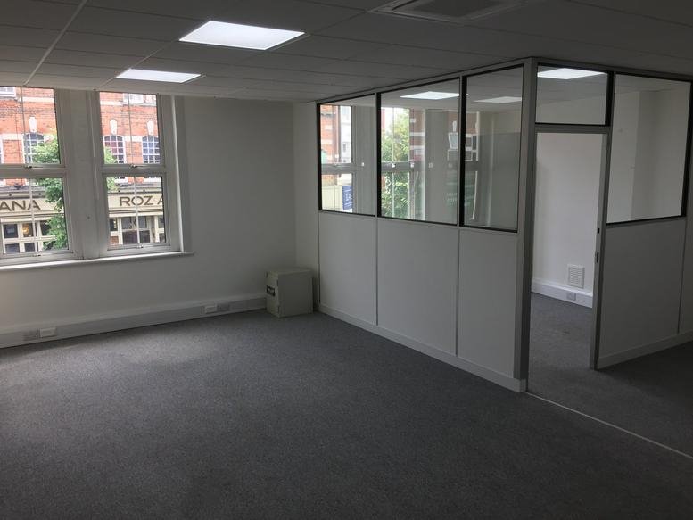 Spacious open-plan office area with grey carpets and a glass-partitioned private room.