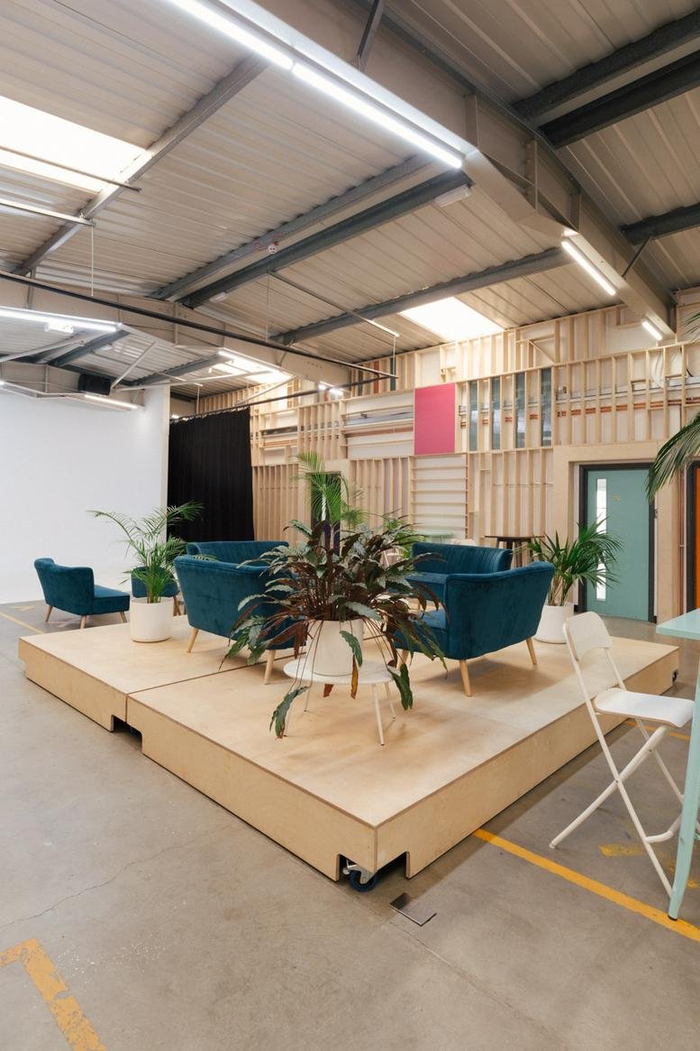 Spacious communal breakout area at 5 Hancock Road with blue velvet sofas on a wooden platform.