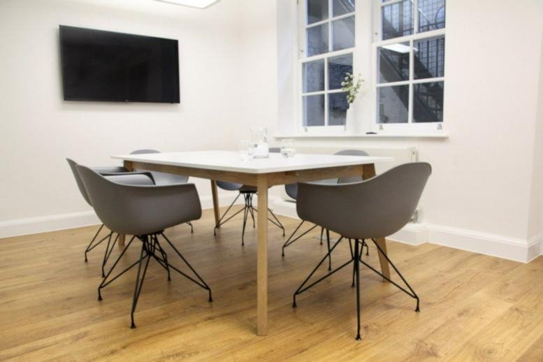 Modern meeting room with a wall-mounted TV and grey bucket-style chairs.