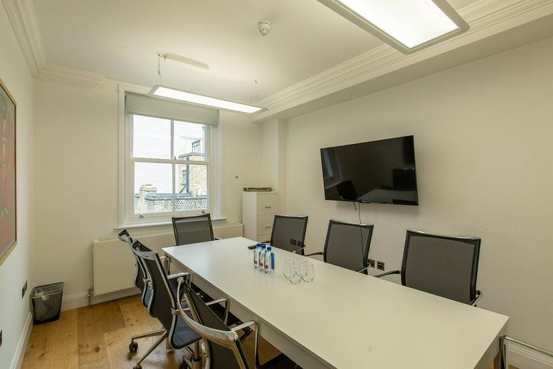 Professional boardroom featuring a long white table, black mesh chairs, and a large monitor.